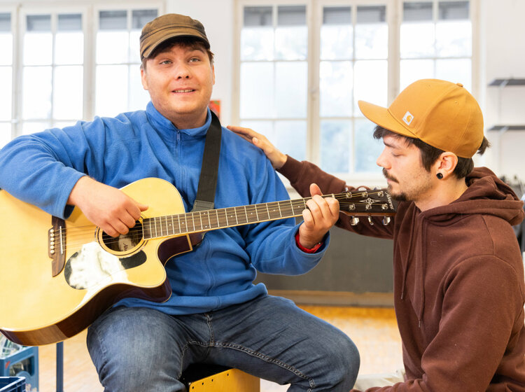 Ein Mann spielt Gitarre, ein anderer hört zu.