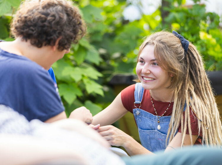 Eine junge Frau mit Dreadlocks unterhält sich mit einer Person im Freien